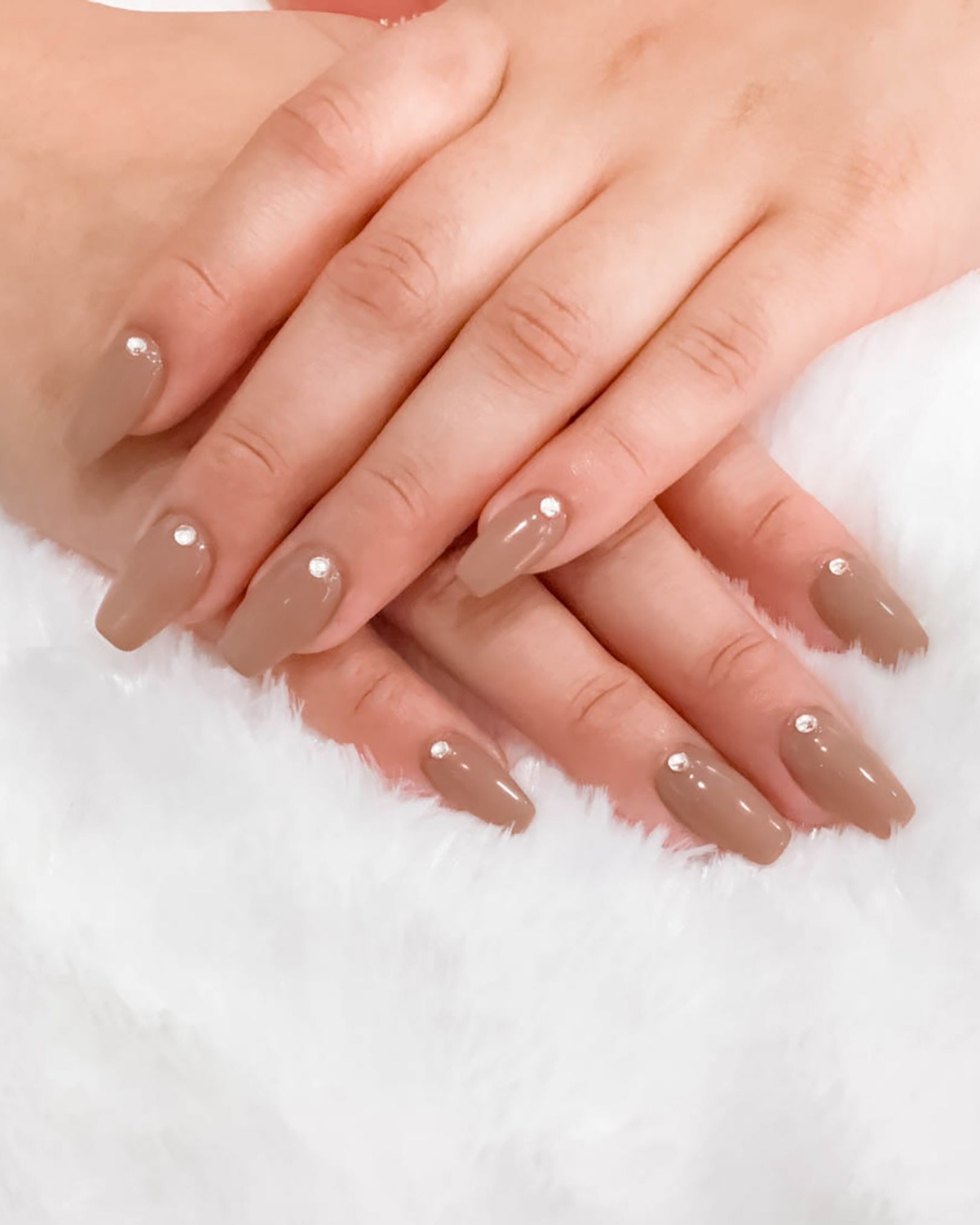 Coffin-shaped nails in elegant nude with small crystal accents at the cuticle, minimalist and clean style