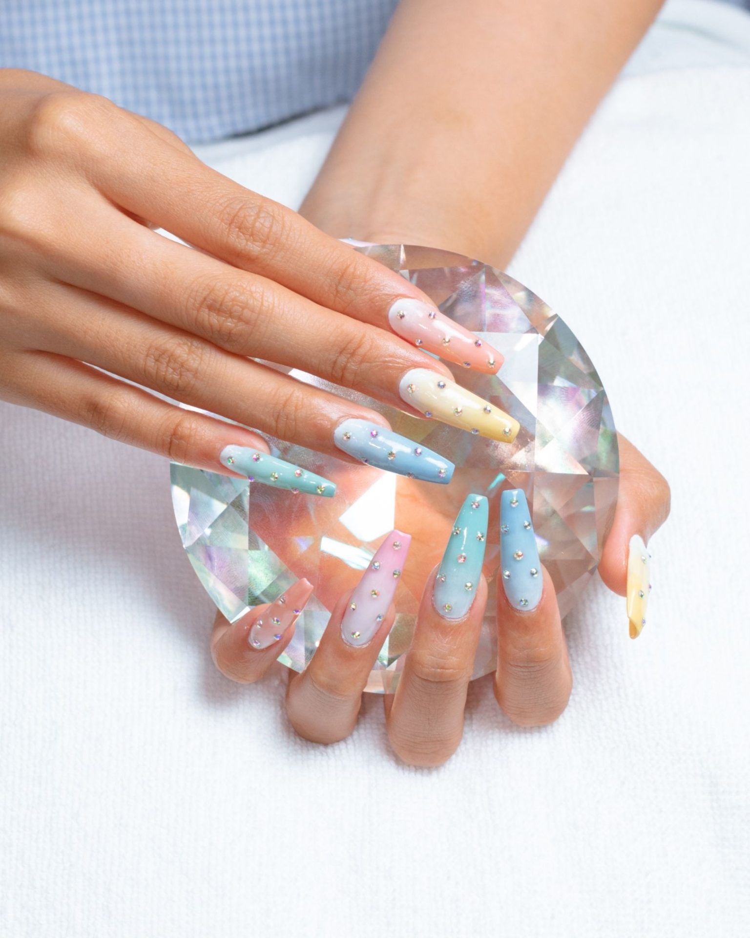 Long pastel nails with rainbow ombre, decorated with scattered crystals across the whole nail