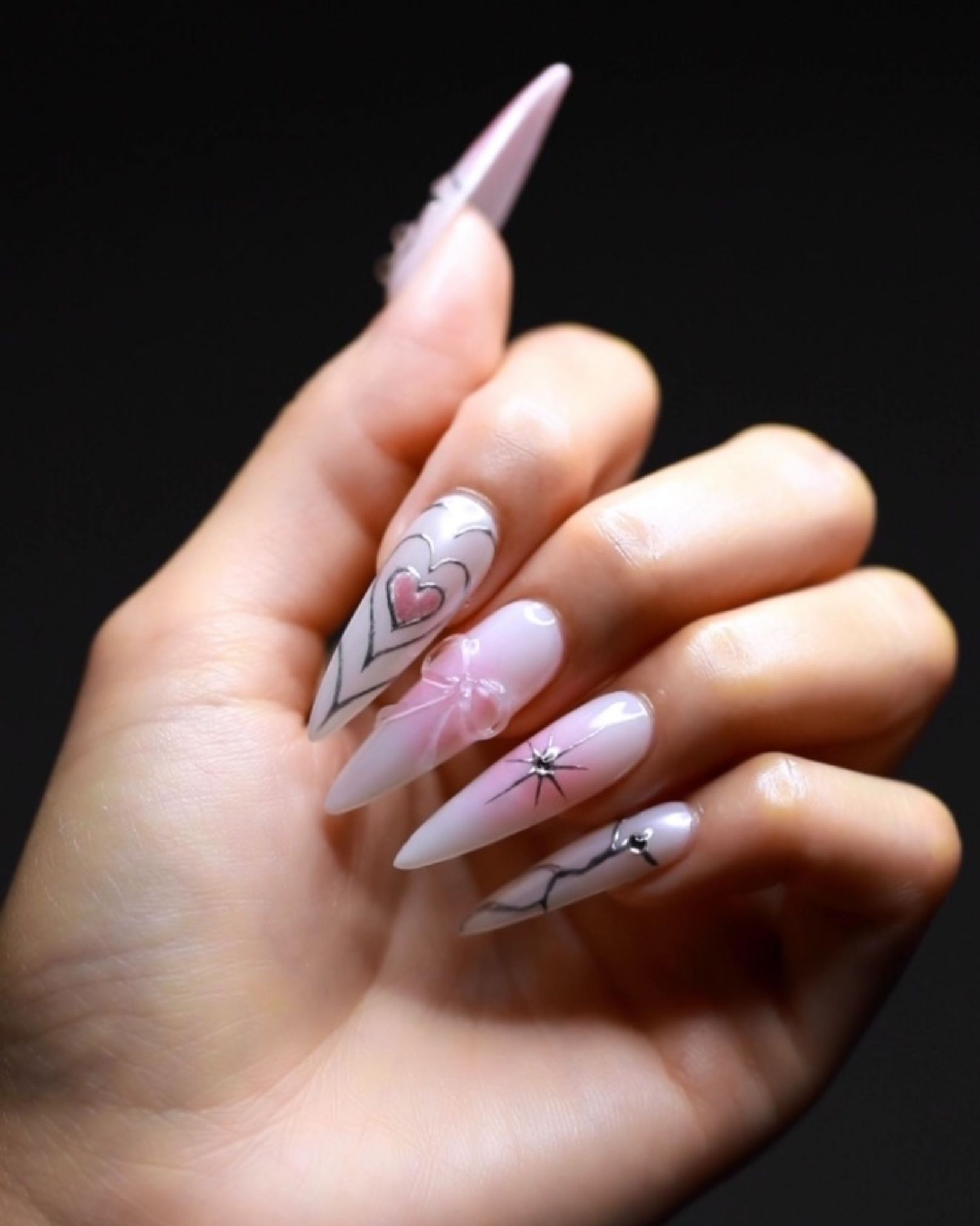 Long stiletto nails painted with pink hearts, 3D ribbon bows, and scattered stars for a standout fashion look