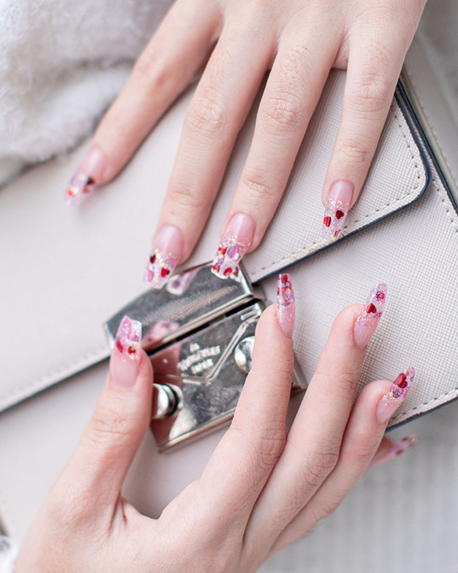 Long pink toned nails decorated with heart-shaped glitter