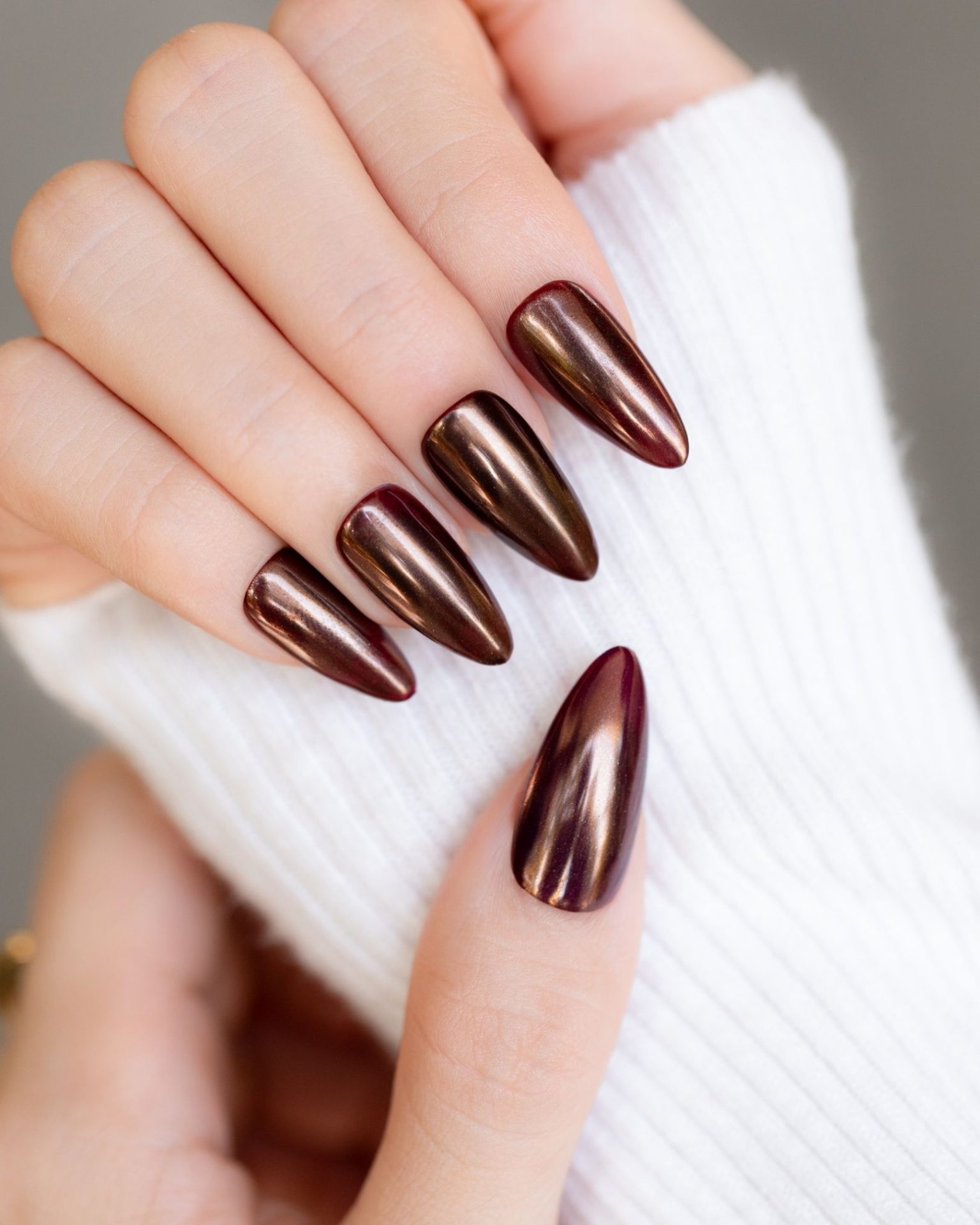 Long almond nails in metallic deep bronze brown for a glossy, light-reflecting luxe look