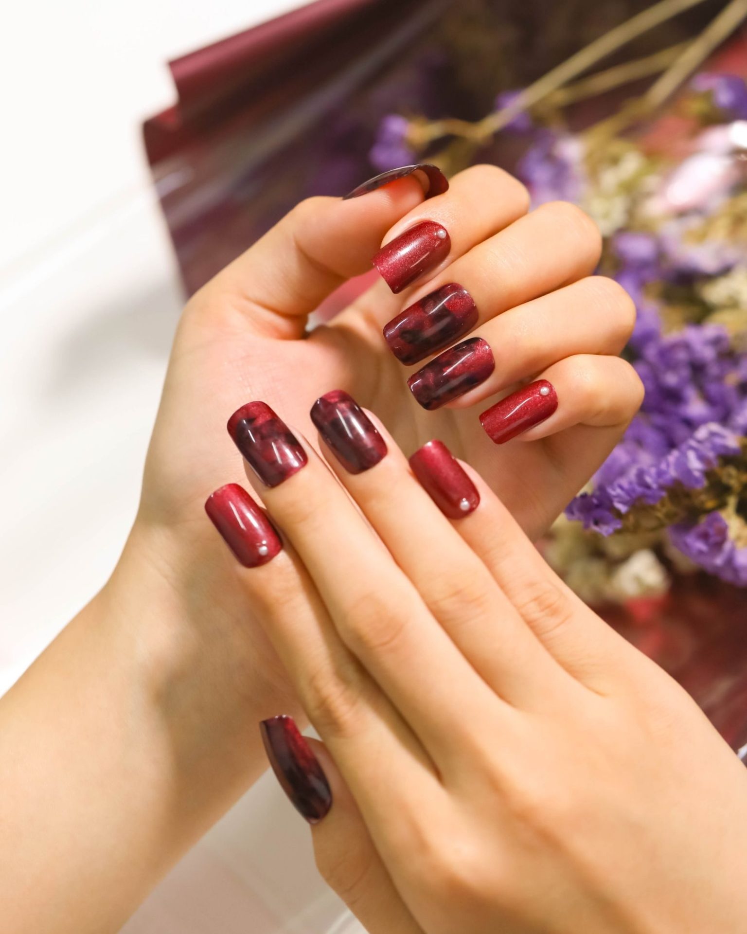 Square-shaped nails in deep red Cat Eye pattern decorated with small pearls, luxurious touch