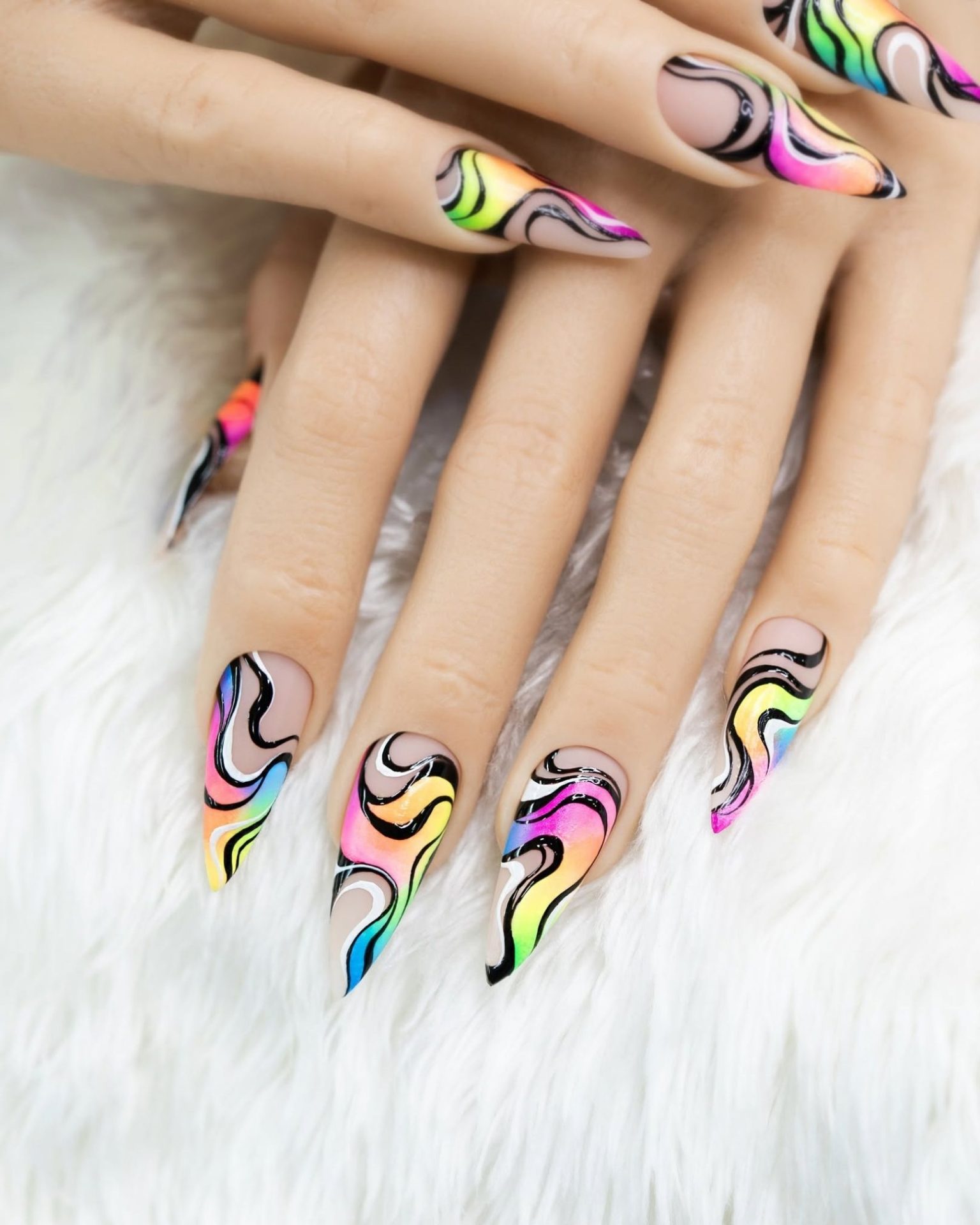 Stiletto nails painted with abstract rainbow wave pattern on a nude base, artistic style