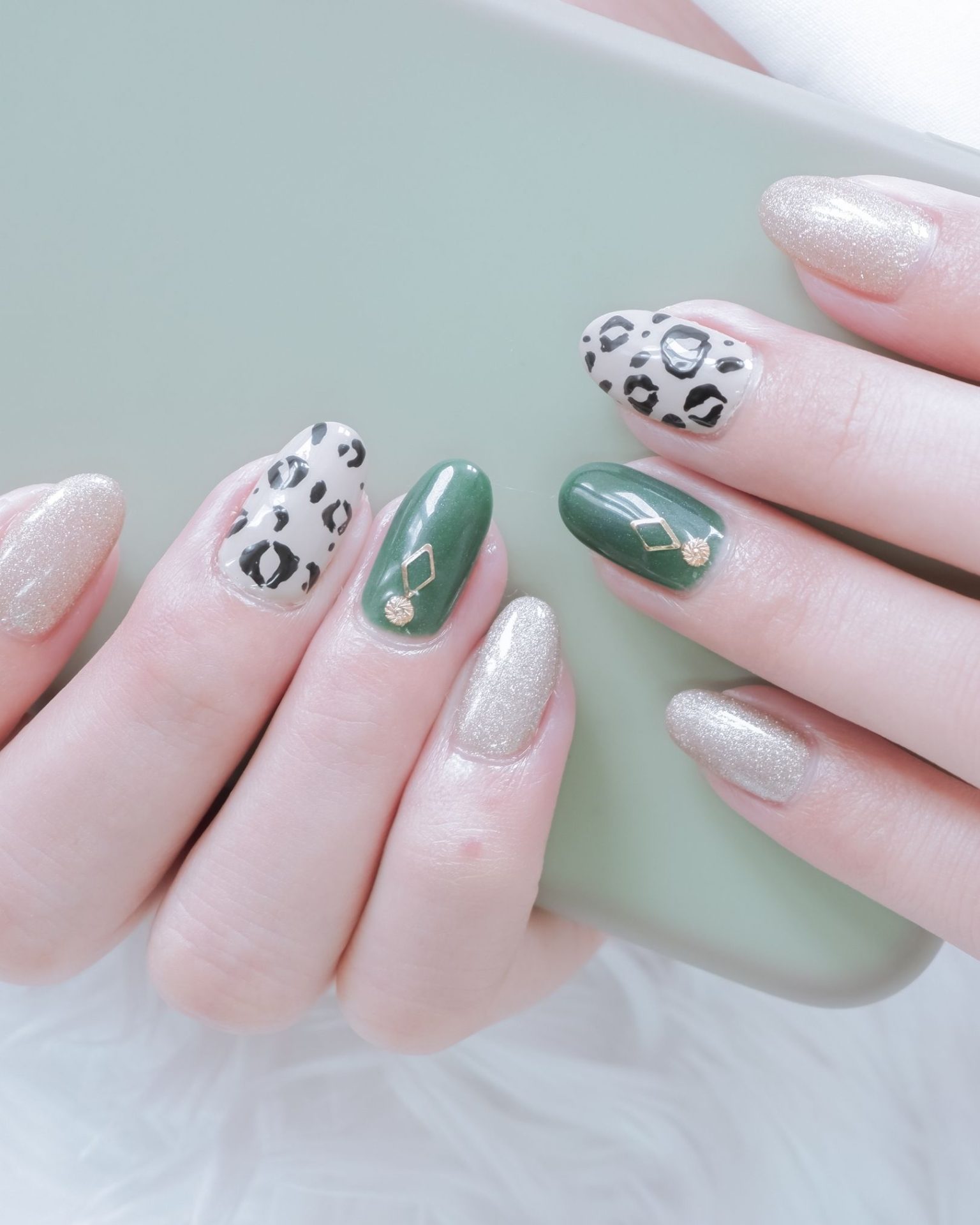 Deep green and leopard print nails decorated with small gold jewelry accents, luxurious modern style