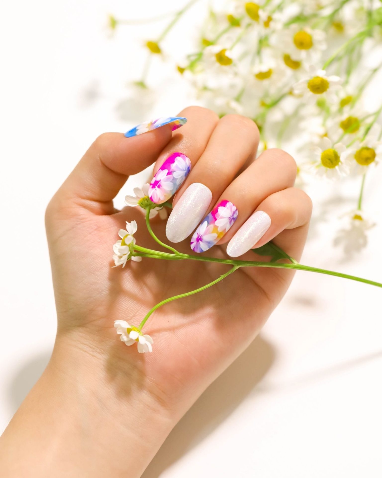 Pearl-white toned nails painted with bright daisy flower designs