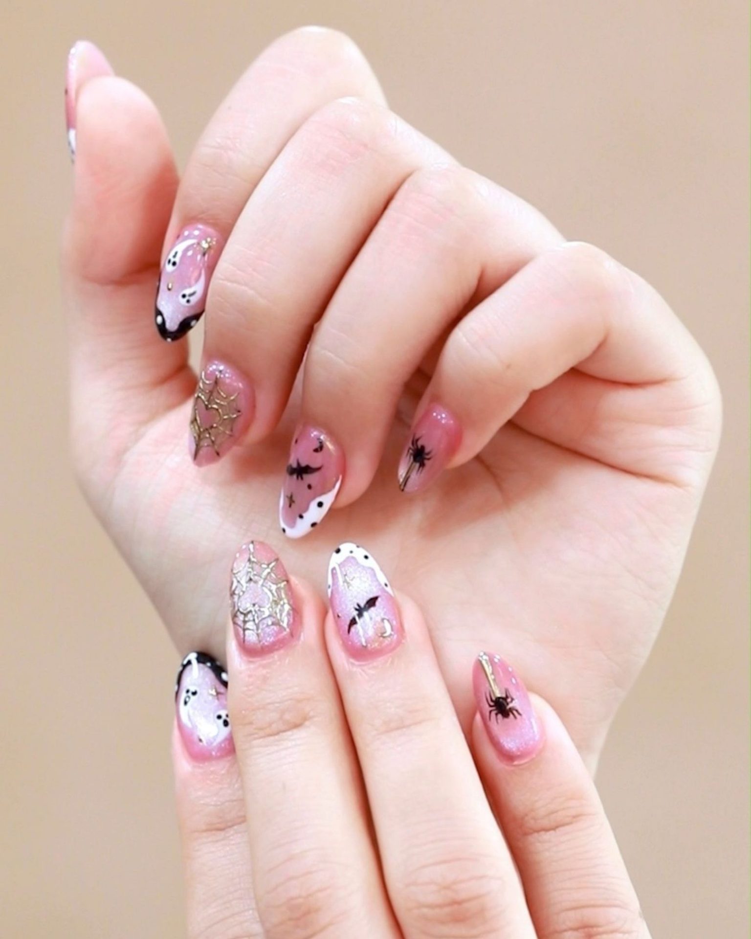 Pink glitter toned nails painted with cute little ghost and gold spiderweb design, kawaii Halloween style