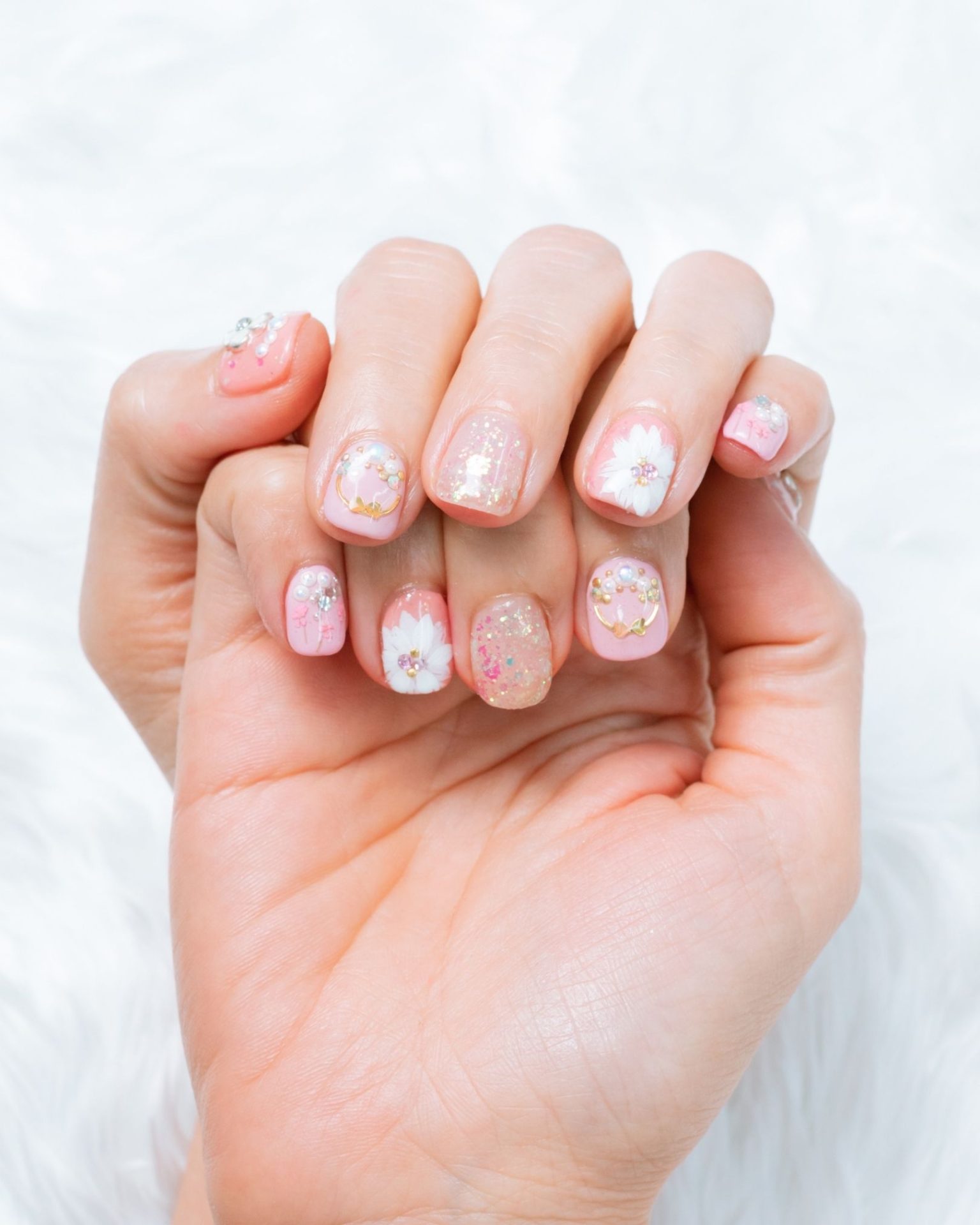 Light pink and white toned nails painted with flowers and decorated with pearls and crystals, sweet style
