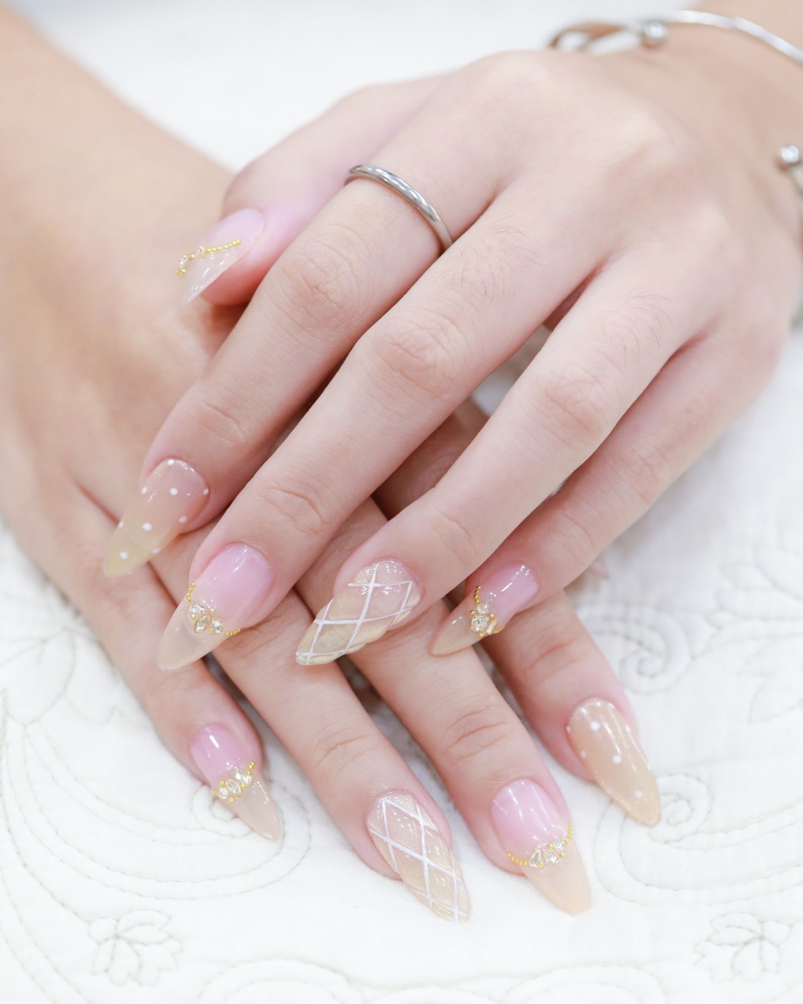 Nude toned nails decorated with white grid pattern and gold crystals at the cuticle, clean elegant style