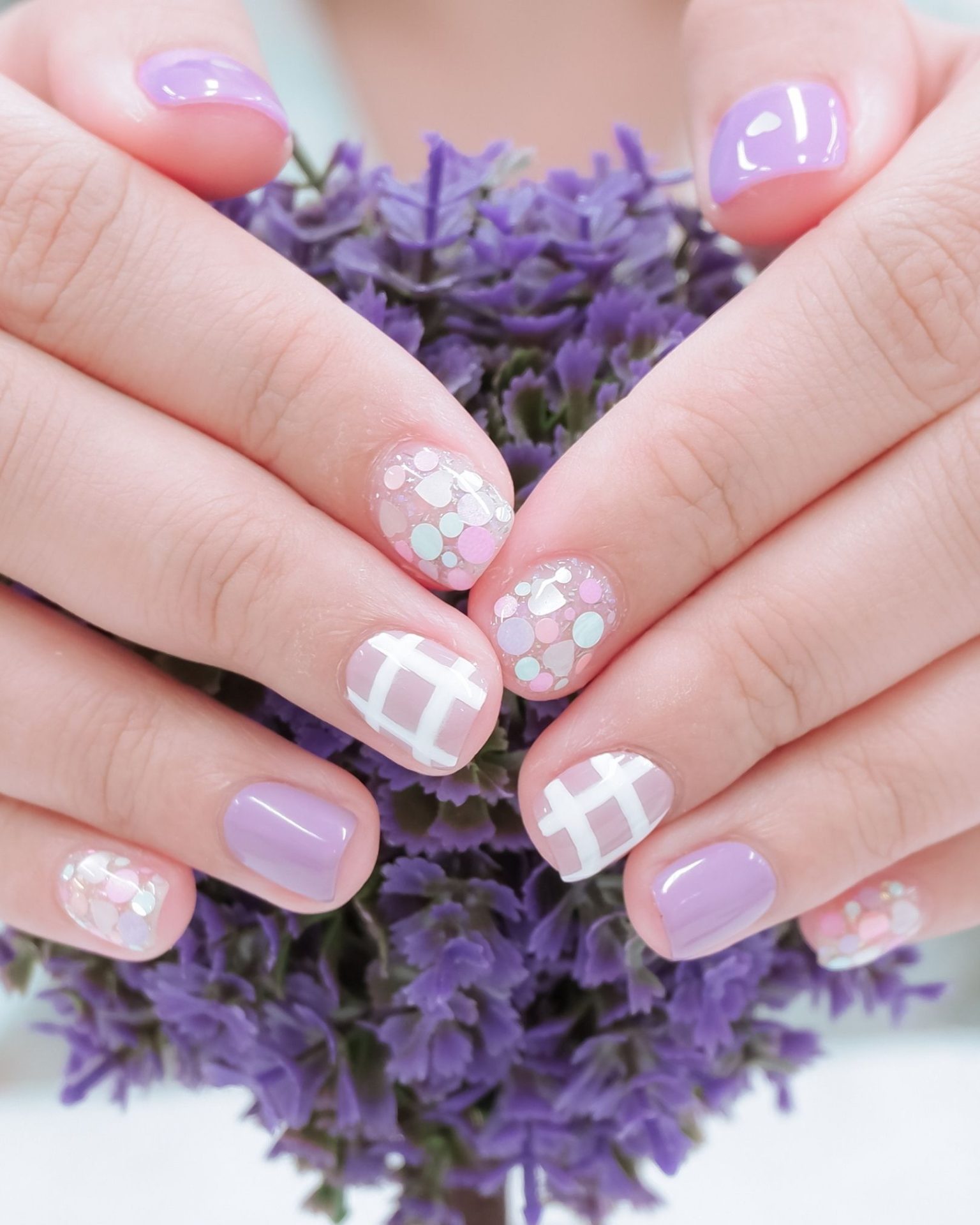 Pastel purple toned nails painted with grid pattern and colorful dots, cute sweet minimalist style